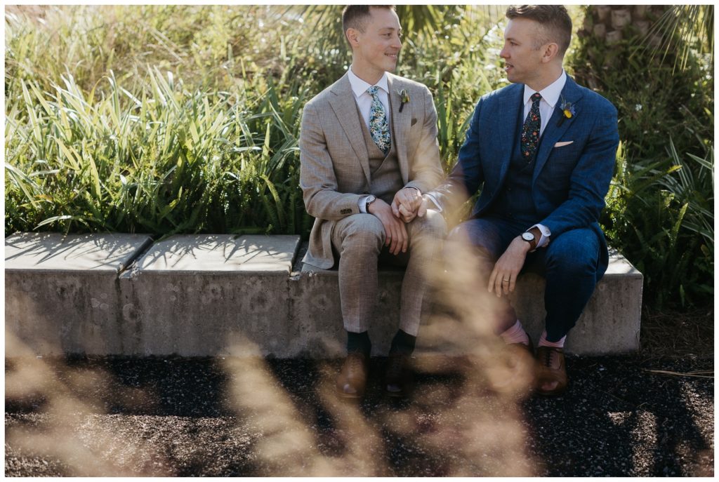 The grooms sit in the park before their Tigermen Den wedding ceremony