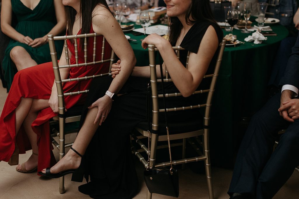 One wedding guest rests her hand on another's leg.