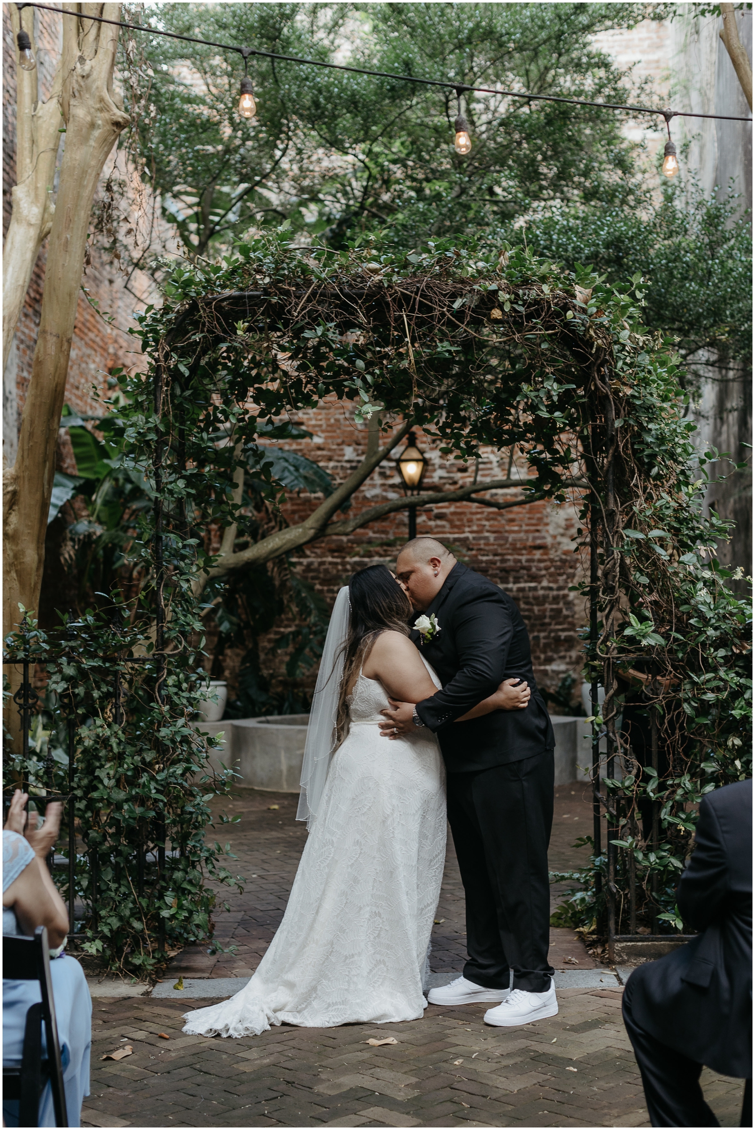 A man and woman kiss under an arch at their micro wedding.
