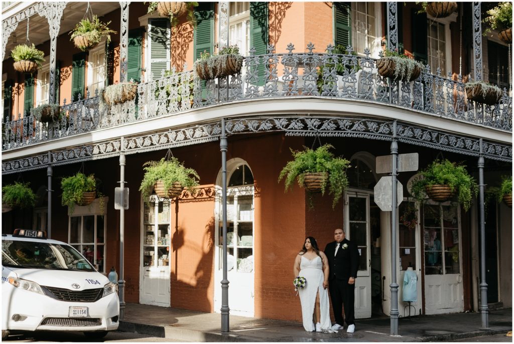 A couple walks through the French Quarter under hanging ferns.