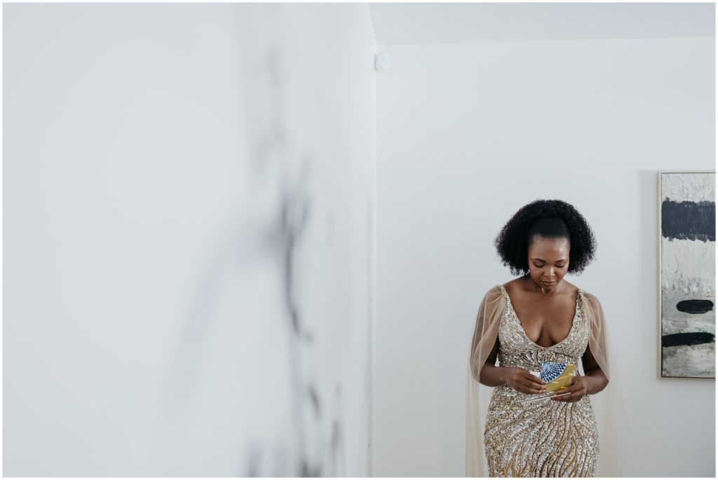 Isatu stands against a white wall in a gold wedding dress.