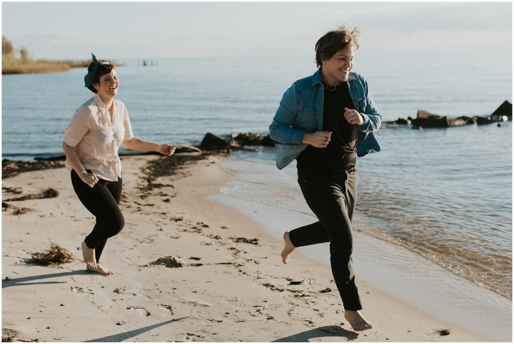 Britt and Em run along the shore in their lakefront engagement photo.
