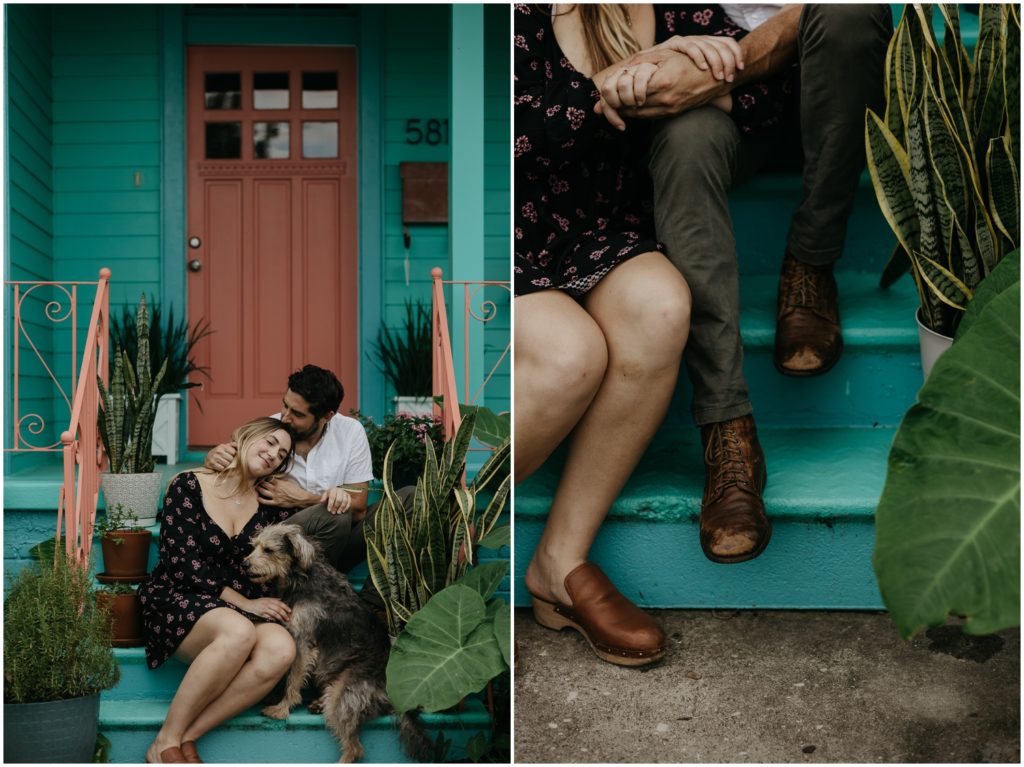 A couple sits on the porch of a blue house with their dog.