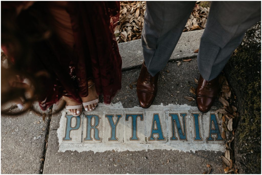 Two people stand on the sidewalk tiles for Prytania Street in a New Orleans engagement photo session.