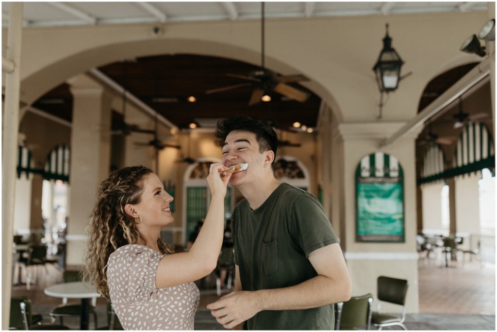 A woman feeds her fiance a beignet at a New Orleans engagement photo session.