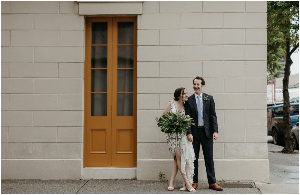 Michael and Marissa stand in front of a white building in New Orleans CBD on their rainy wedding day.