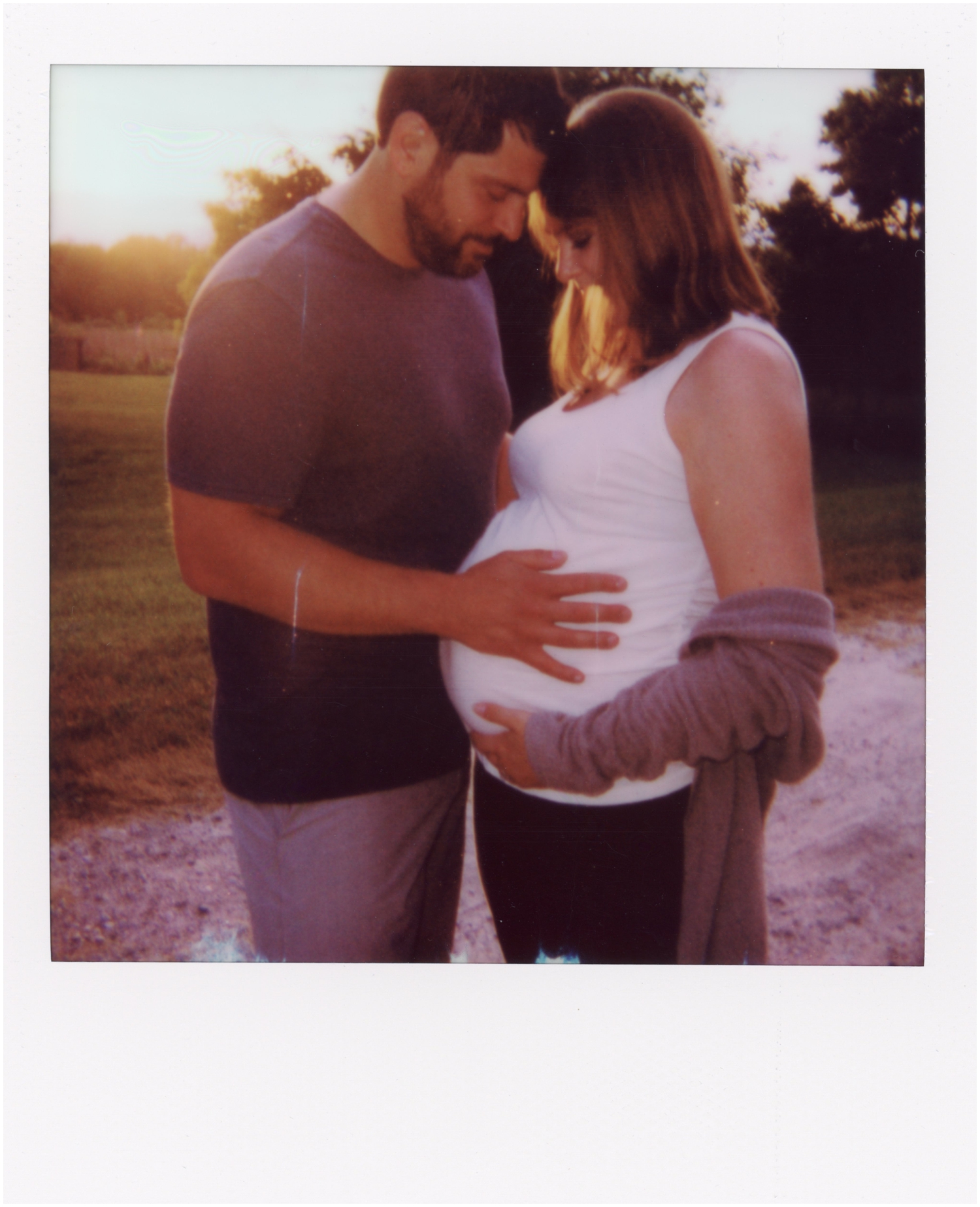 Andrew puts his hand on Stephanie's stomach in a Polaroid maternity photo.