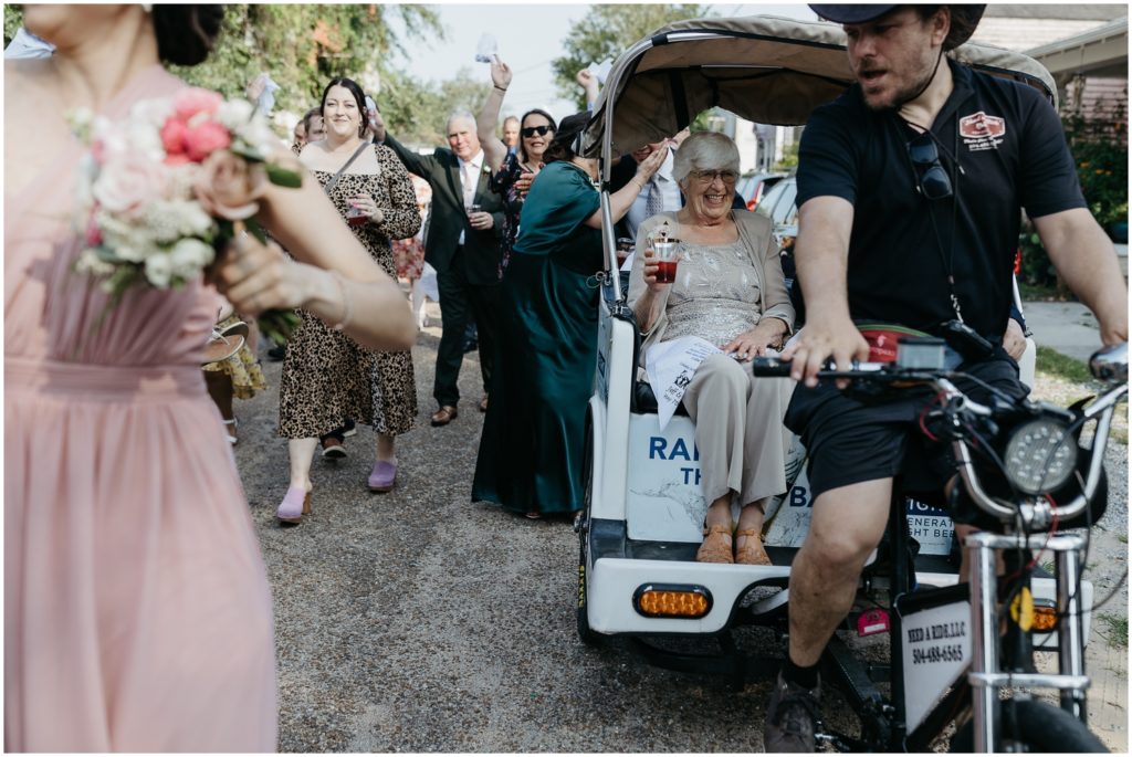 A pedicab pulls a wedding guest beside the second line.