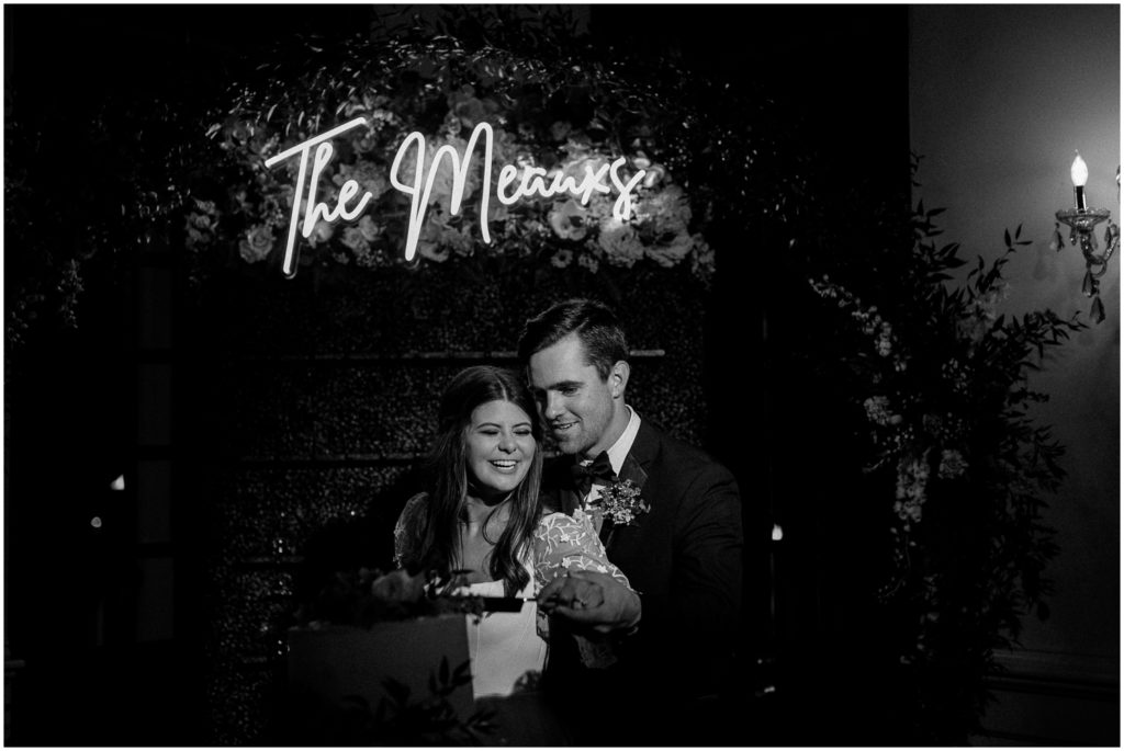 The bride and groom cut their wedding cake under a neon light at Rip Van Winkle Gardens.
