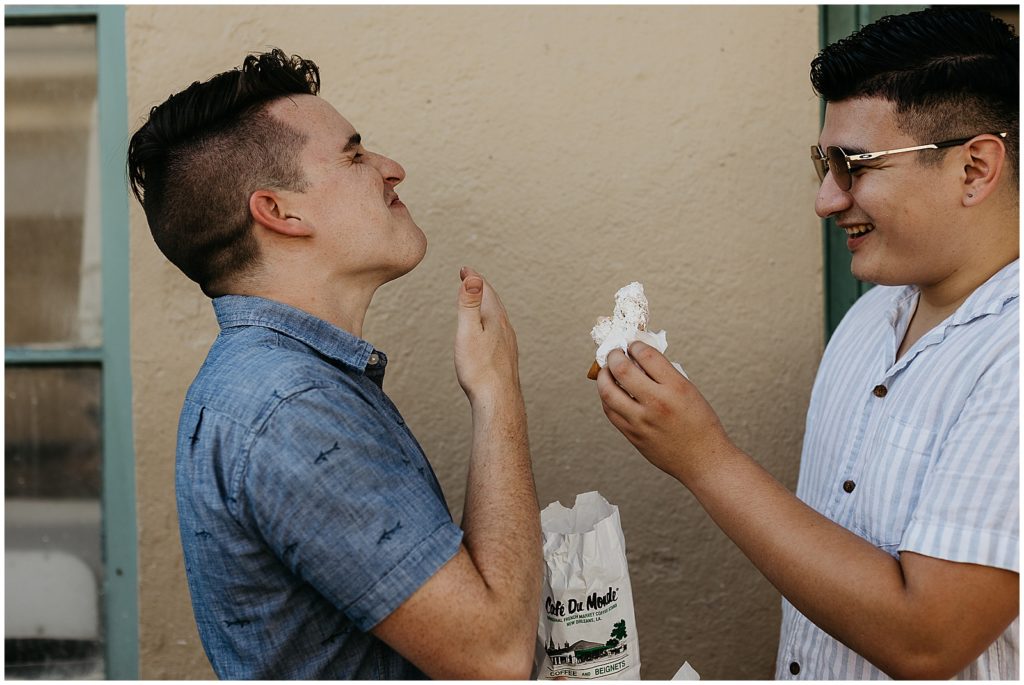 Enrique and Caleb laugh as they eat beignets in French Quarter engagement photos.