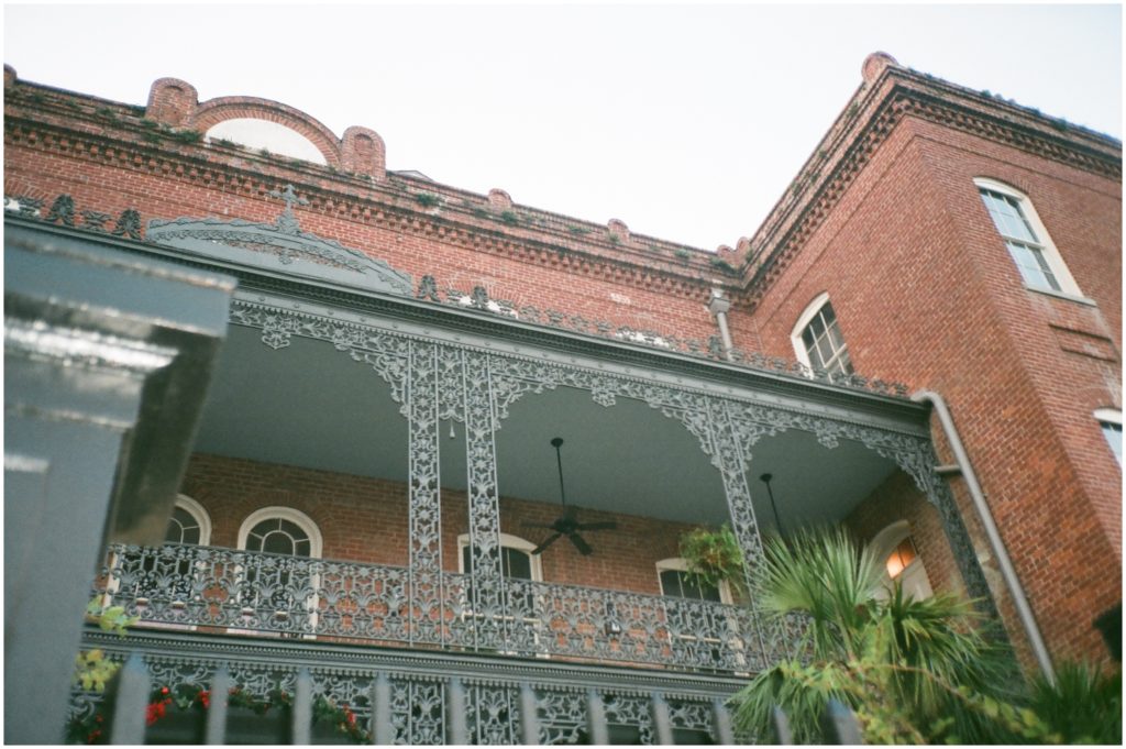 A brick building has an iron balcony with elaborate bars.