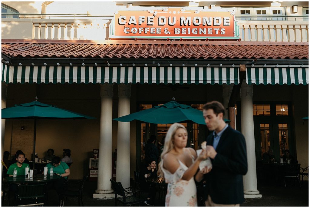 An engaged couple eats beignets out of a white bag at Cafe Du Monde.