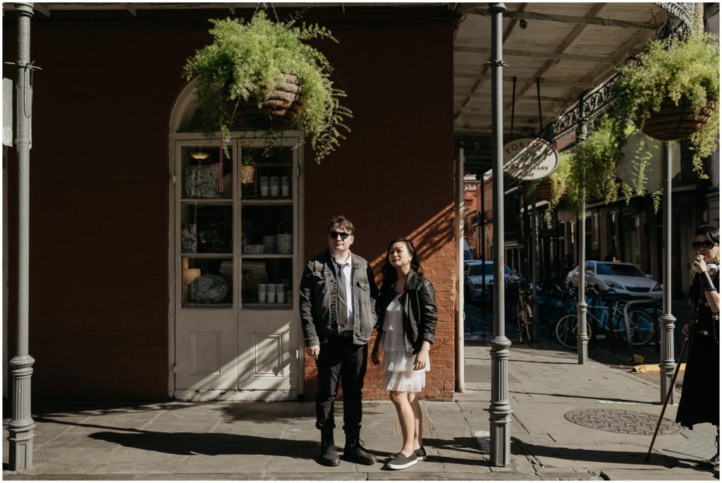 Theresa and Nathaniel stand under hanging ferns by an orange building.