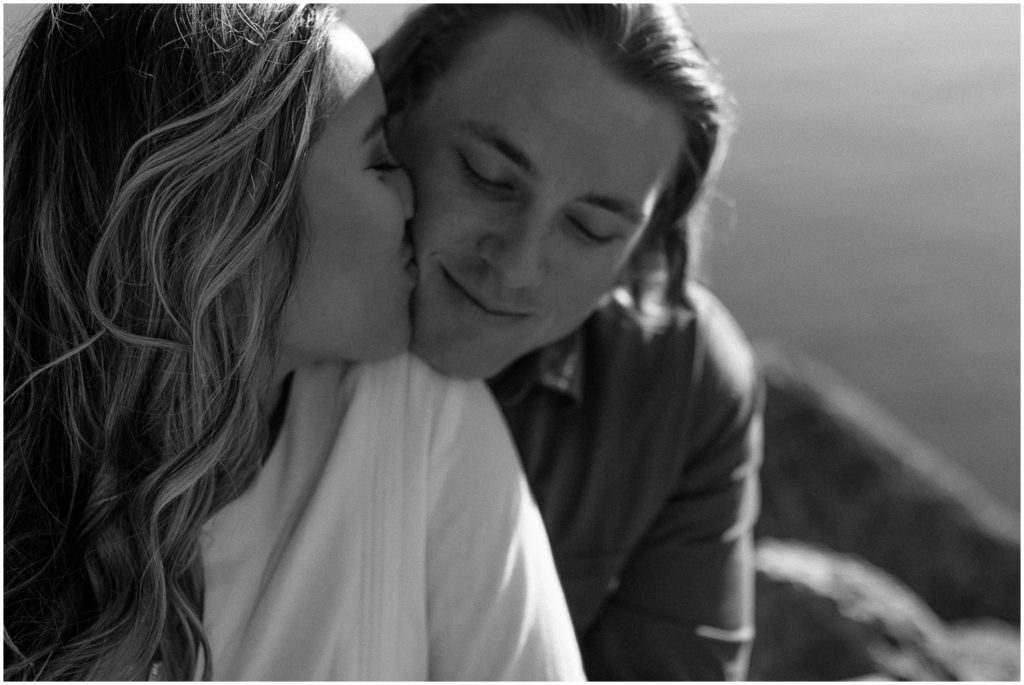 Jeannie kisses Jacob's cheek in sunset engagement photos beside Lake Pontchartrain.