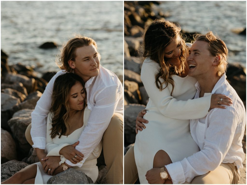 A couple sits for sunset engagement photos on boulders beside Lake Pontchartrain.