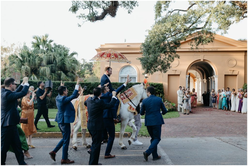 A groom's wedding party dances as he rides a horse towards an Indian wedding ceremony in New Orleans City Park.