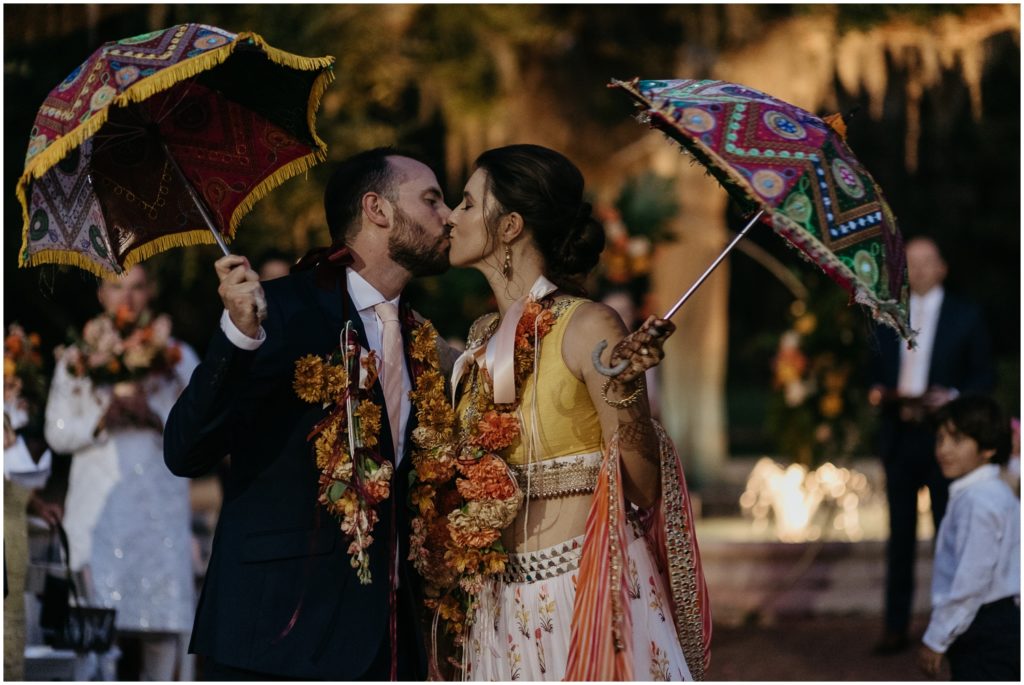 A bride and groom kiss at the end of the aisle after their Indian and Colombian wedding ceremony.