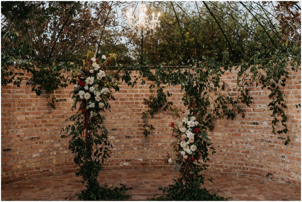 A floral wedding arch stands in front of a brick wall.
