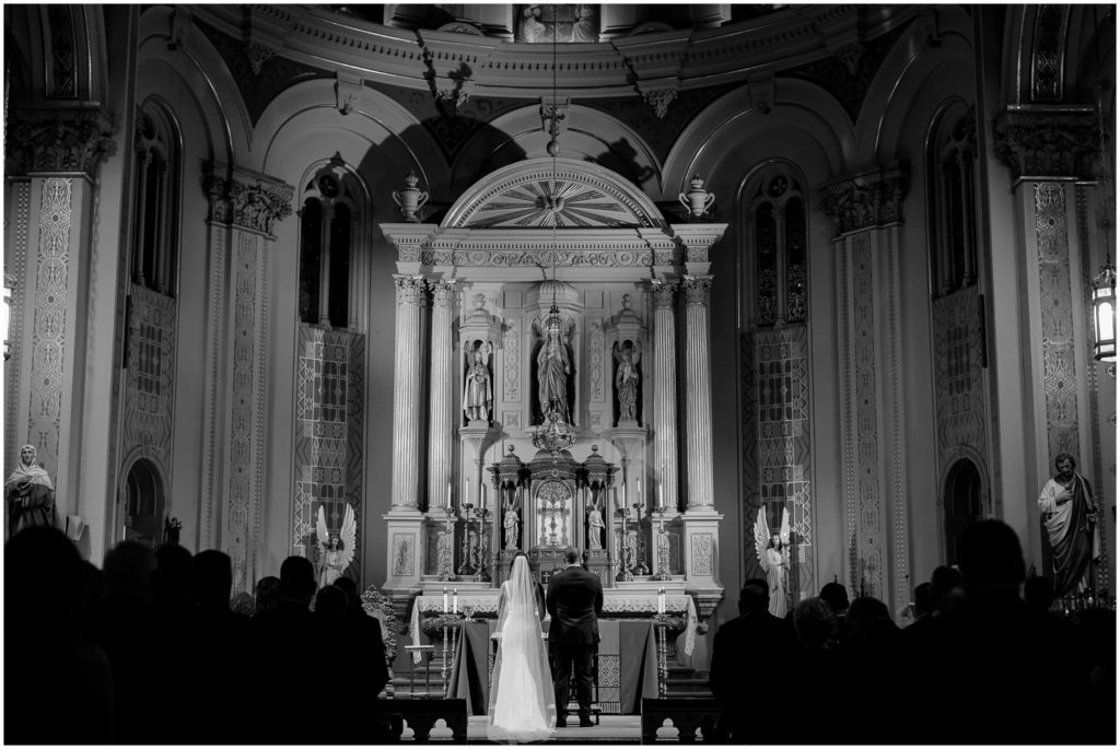 A bride and groom stand for a wedding ceremony in a large Catholic church.