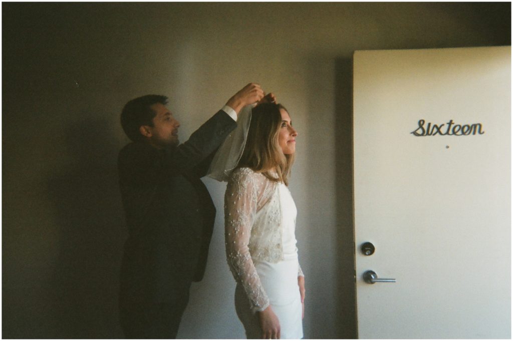 A groom helps a bride put on a veil for an elopement in New Orleans.