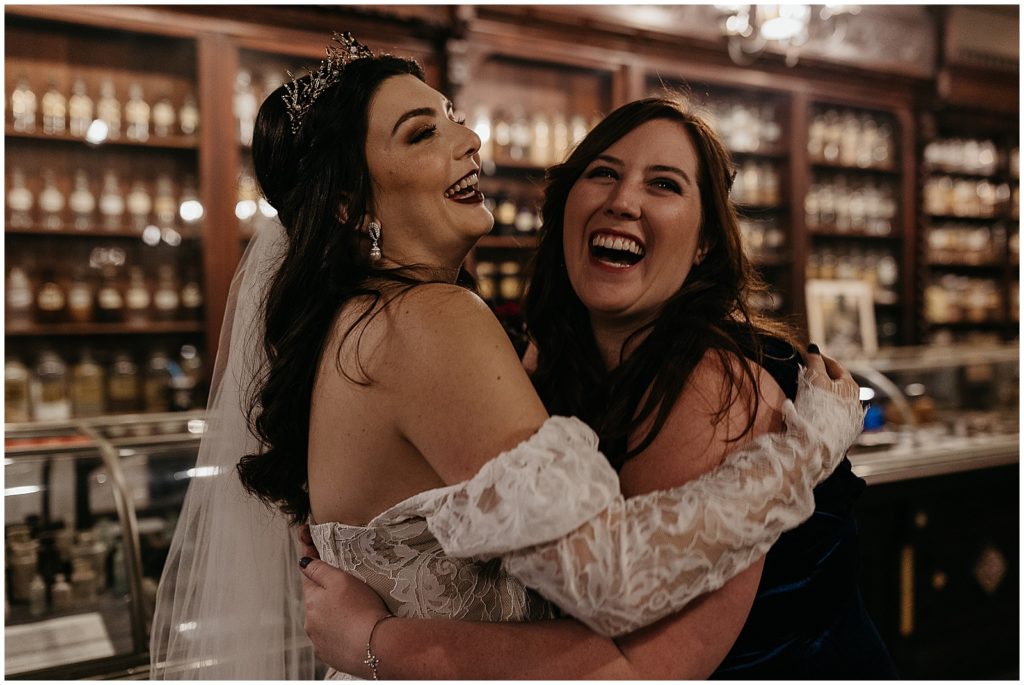 A bride embraces a friend and laughs inside the Pharmacy Museum.