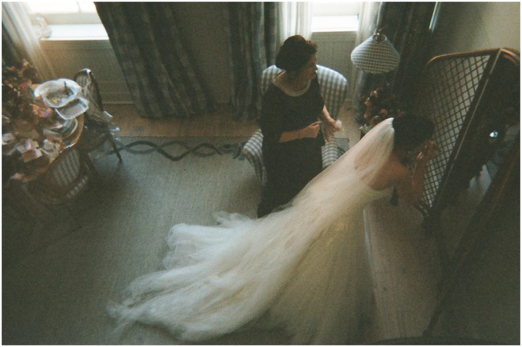 A bride puts on lipstick with her veil trailing behind her on the hotel carpet.