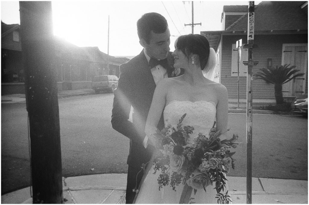 Steven puts his arms around Mary on a New Orleans sidewalk while she holds her bridal bouquet.