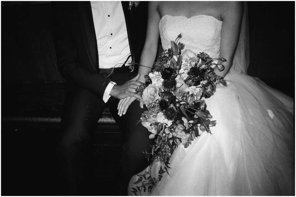 A bride and groom hold hands in a black and white wedding photo.