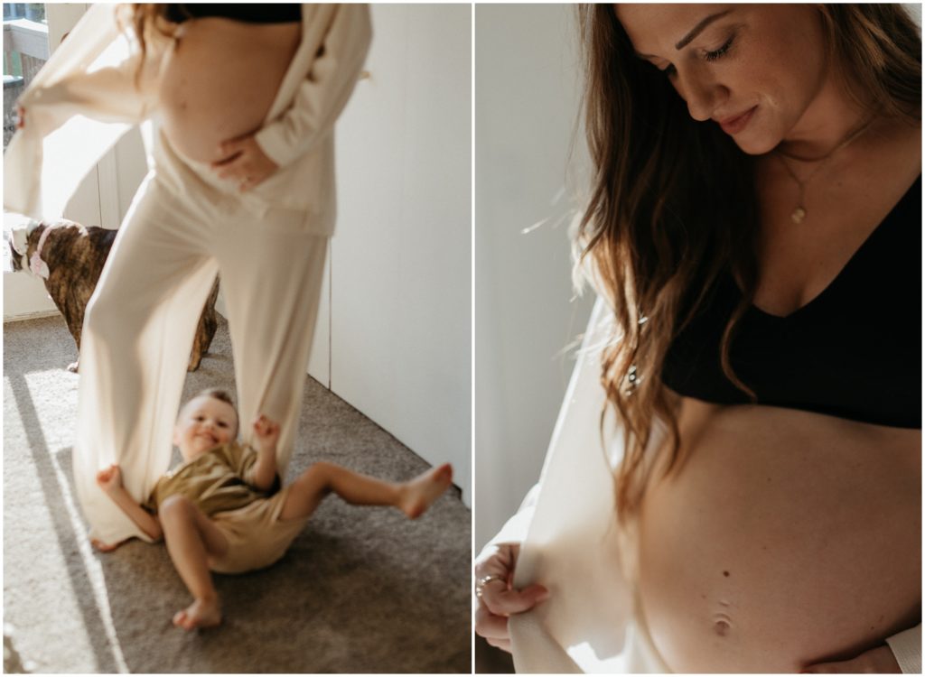 A woman's son rolls on the floor beneath her as she pulls her shirt away from her pregnant belly.